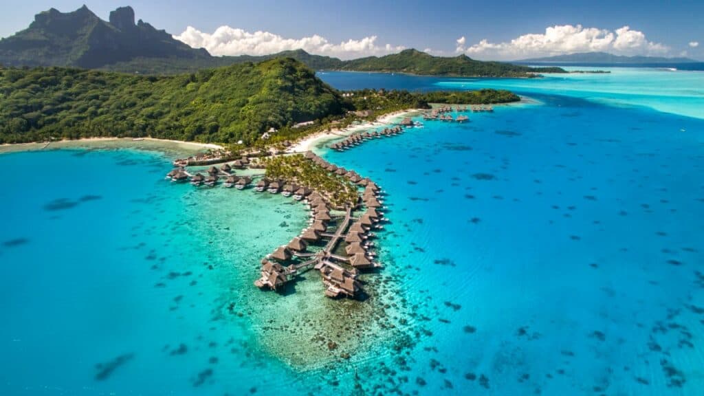 Aerial view of Conrad Bora Bora Nui  bungalows spanning across the lagoon in blue ocean water