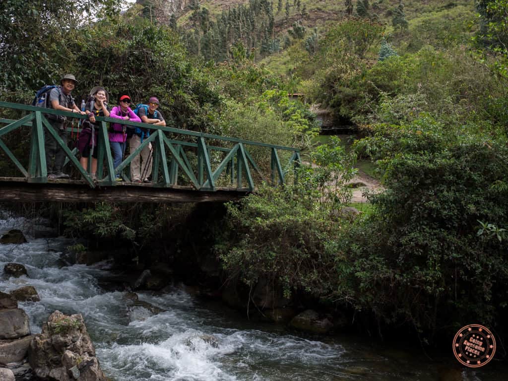 group of friends hiking inca trail on bridge with river underneath